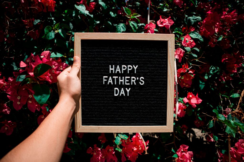 A hand holding a Happy Father's Day sign amid vibrant pink bougainvillea flowers.
